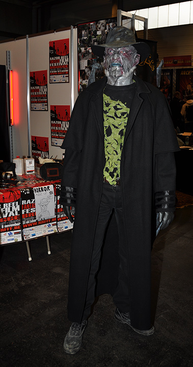 F.A.C.T.S. 2010 — Homme au visage gris habillé et ganté de noir, portant un chapeau, devant un stand de maquillage